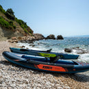Two inflatable kayaks on a pebbly beach with ocean and rocks in the background