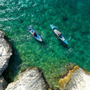 Two kayakers paddling in clear turquoise water near rocky cliffs.